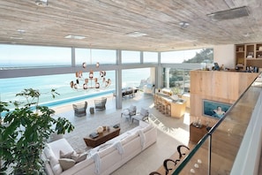 Een ruime woonkamer met een groot raam met uitzicht op de oceaan, een moderne kroonluchter en een gezellige zithoek.