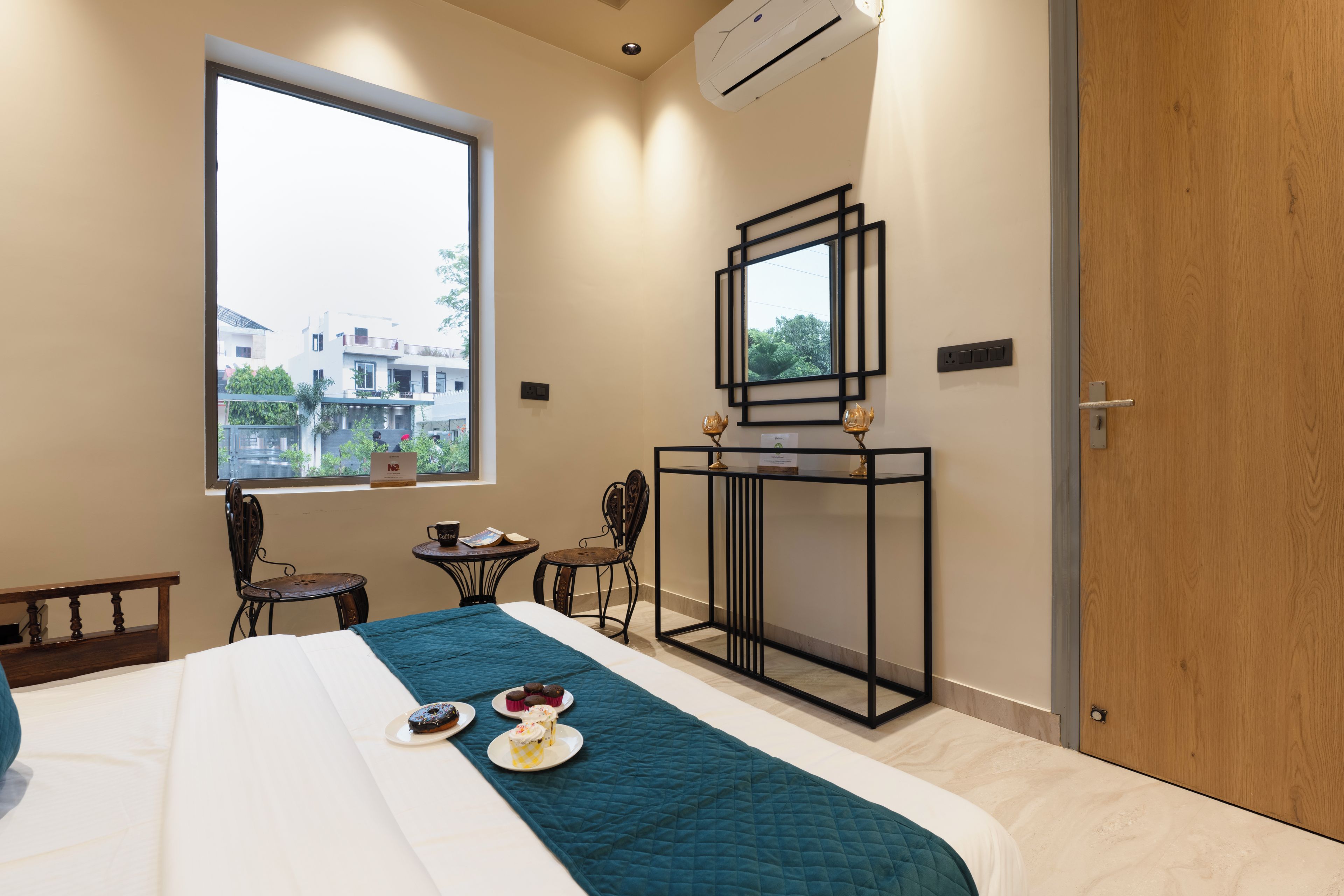 Une chambre d’hôtel avec un lit, une petite table sur laquelle se trouvent une tasse et un livre, une chaise et une fenêtre donnant sur les bâtiments environnants.
