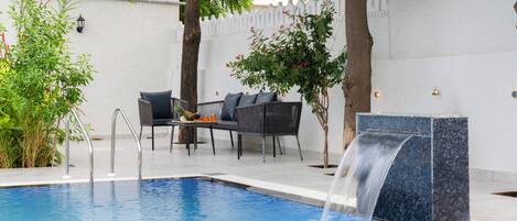 A swimming pool with a waterfall feature, surrounded by outdoor seating and greenery.