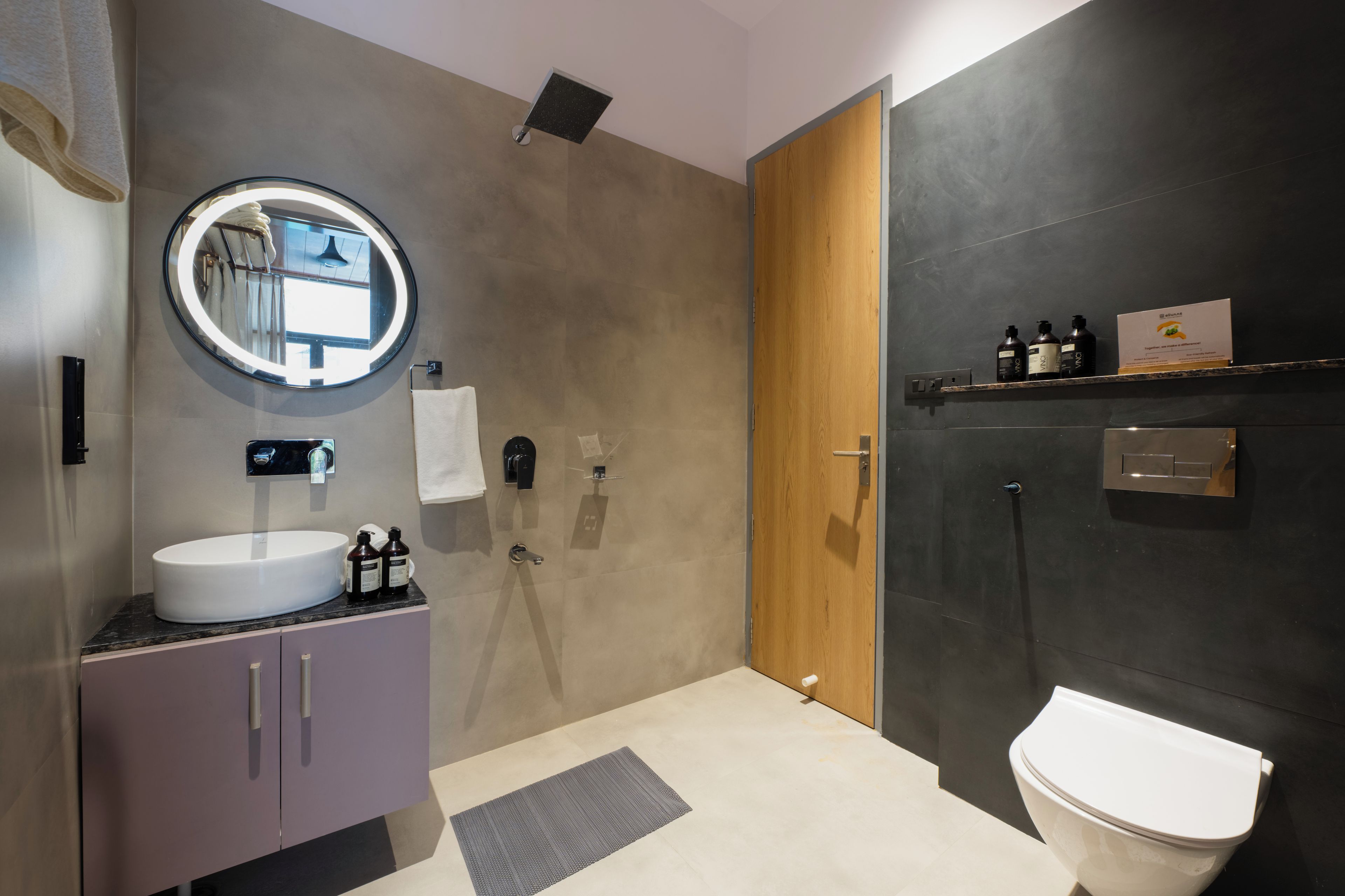 A modern bathroom with a round mirror, a white sink, and a toilet.