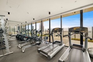 A gym with various exercise equipment, large windows, and a view of the cityscape. - Skyline Serenity 2BR in Melbourne CBD, Sky Gym & Pool (Melbourne)