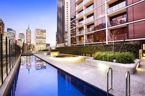 Hotel moderno com piscina no terraço, cercado por edifícios altos.