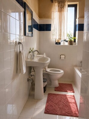 Ein Badezimmer mit Waschbecken, Toilette und Badewanne. Zwei rote Teppiche liegen auf dem Boden.