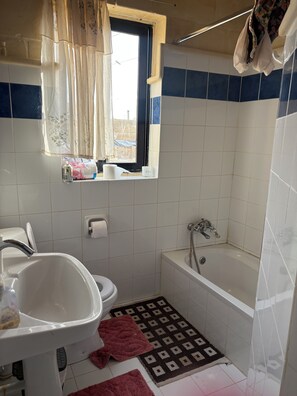 Ein Badezimmer mit Toilette, Waschbecken, Badewanne und einem Fenster mit Vorhängen.