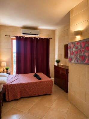 Ein Hotelzimmer mit einem Bett, einem Nachttisch, einer Kommode, einer wandmontierten Klimaanlage und einem Fenster mit Vorhängen.