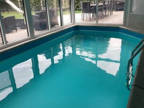 An indoor swimming pool with clear water, surrounded by glass walls and a deck area with outdoor furniture. - 8 Person Holiday Home in Vaeggerlose (Vaeggerlose)