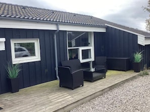 A dark blue building with a tiled roof, a wooden deck, and outdoor furniture including two chairs and a table. - 8 Person Holiday Home in Vaeggerlose (Vaeggerlose)