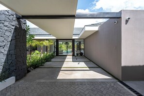 Ein modernes architektonisches Design mit einer Steinwand, einem überdachten Gang und Blick auf einen Poolbereich.