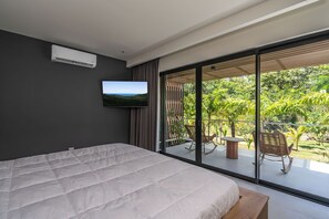 Un dormitorio con una cama grande, televisor y puerta corrediza de vidrio que da a un balcón con mobiliario exterior.