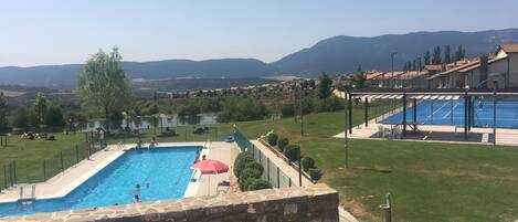 A swimming pool with a stone wall, a red umbrella, and a view of a residential area with houses and mountains in the background.