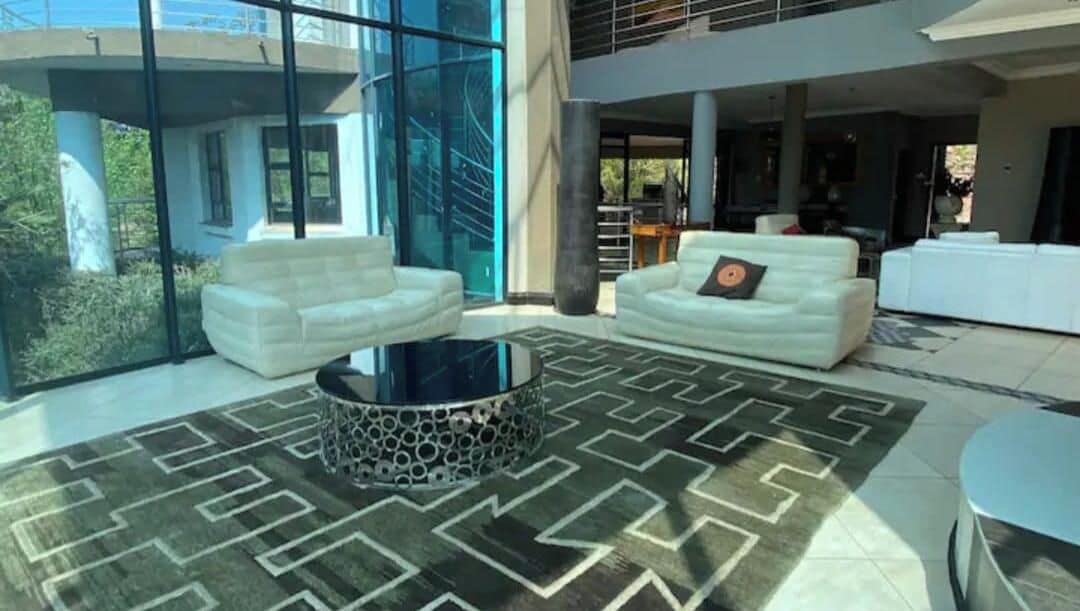 A spacious living area with a modern design, featuring a large glass wall, white sofas, and a patterned rug.