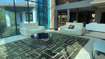 A spacious living area with a modern design, featuring a large glass wall, white sofas, and a patterned rug.