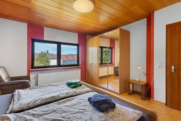 A hotel room with a bed, a chair, a small table, and a mirror.