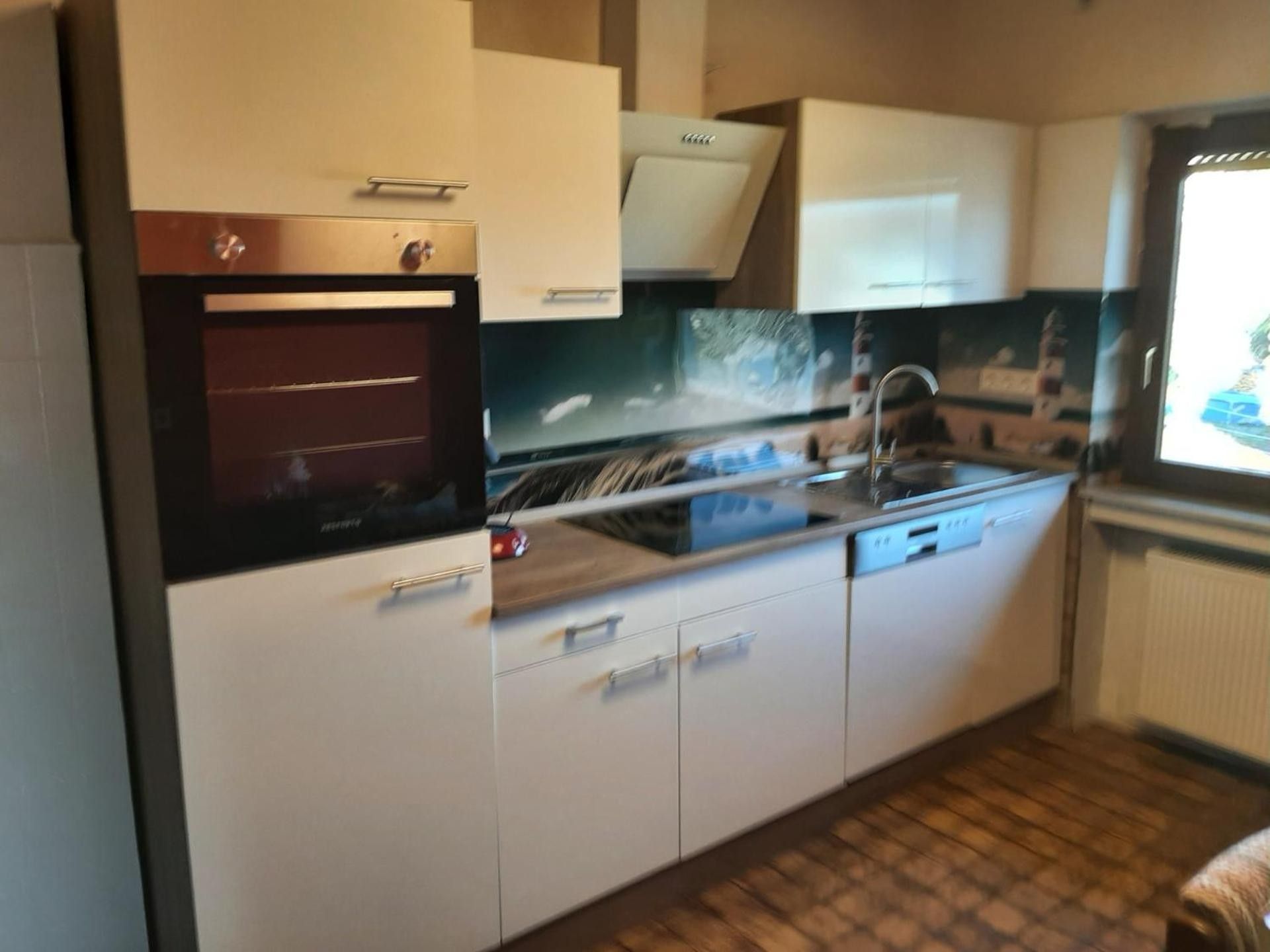 A compact kitchen with a built-in oven, a sink, and a window.