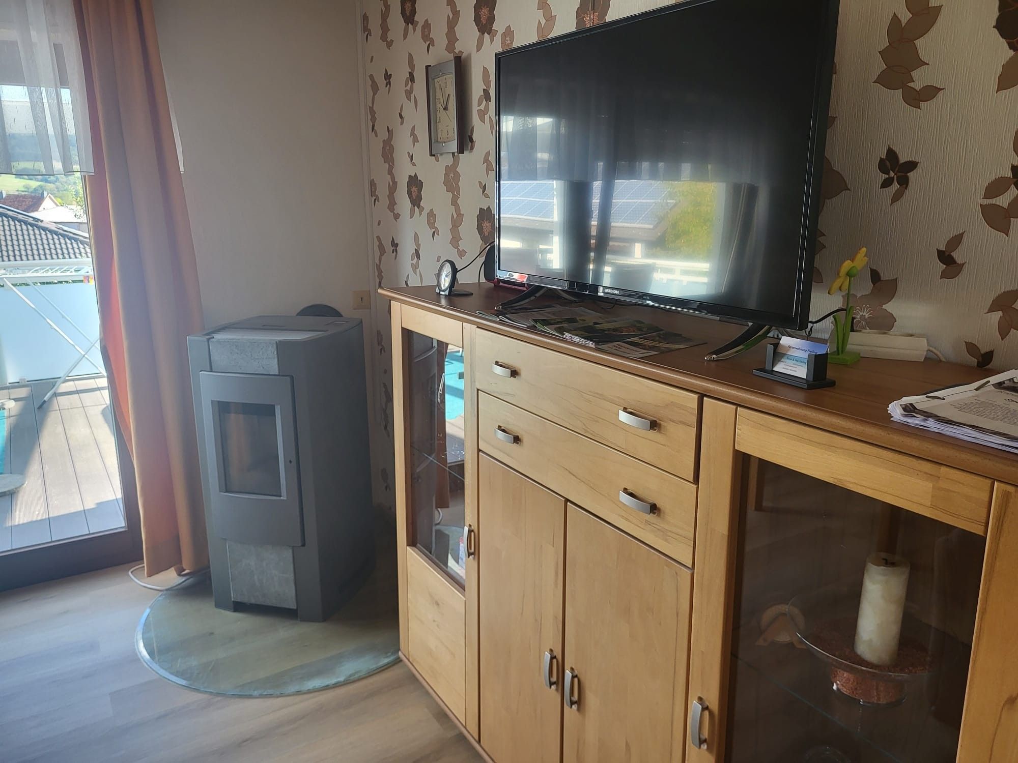 Ein Zimmer mit einem Holzkasten, einem Fernseher, einem kleinen Heizgerät und einem Fenster mit Vorhängen.