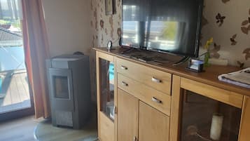 Ein Zimmer mit einem Holzkasten, einem Fernseher, einem kleinen Heizgerät und einem Fenster mit Vorhängen.