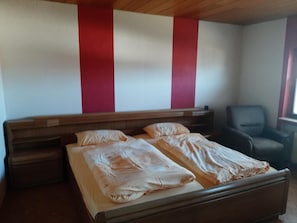 A bedroom with a bed, a chair, and a wooden headboard. - Apartment 'Freiling' with Balcony and Wi-Fi (Dautphetal)
