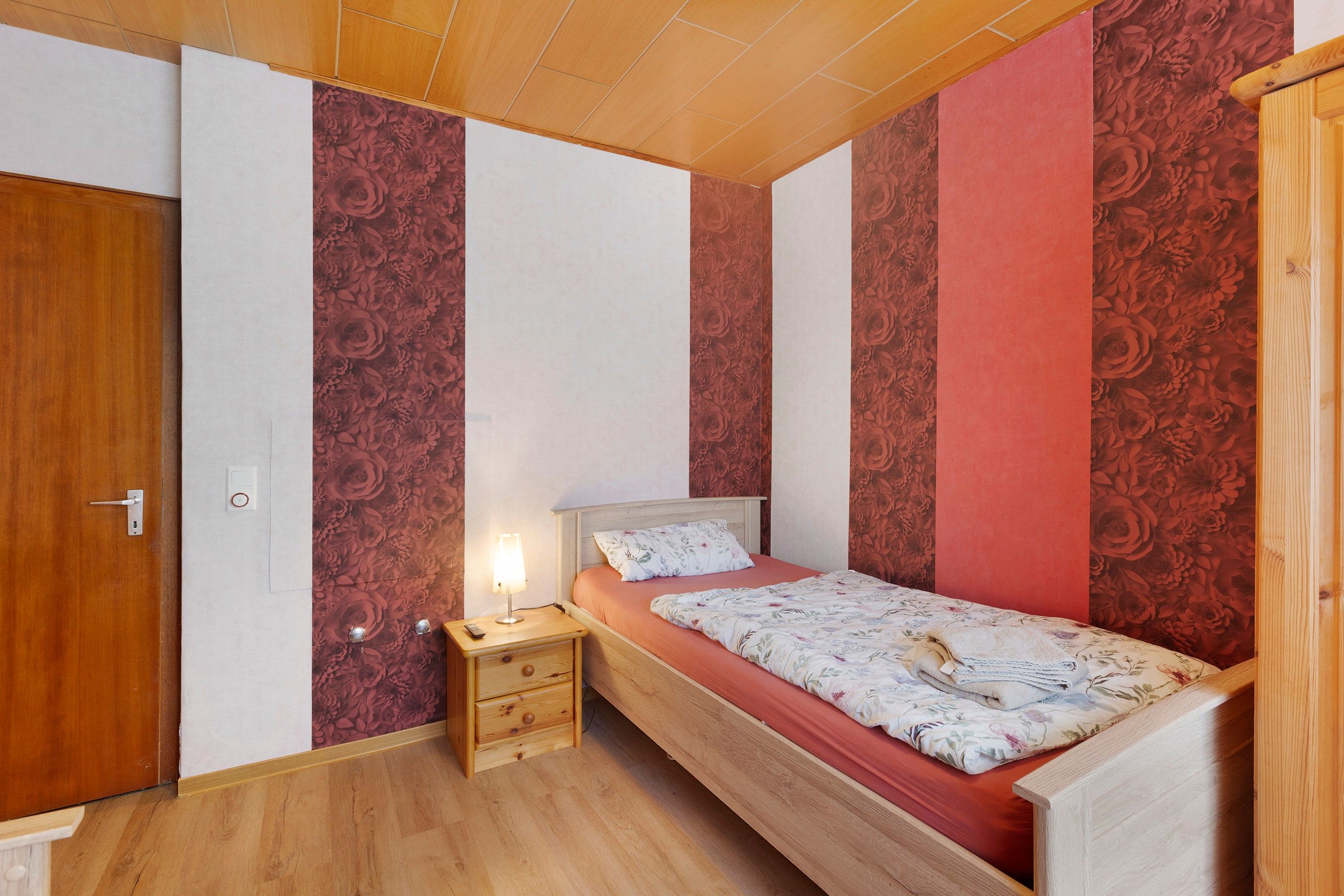 Ein Schlafzimmer mit einem hölzernen Bett, einem Nachttisch und einer Wand mit floralem Wandpapier.