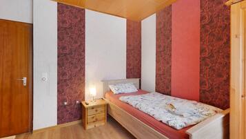 Ein Schlafzimmer mit einem hölzernen Bett, einem Nachttisch und einer Wand mit floralem Wandpapier.