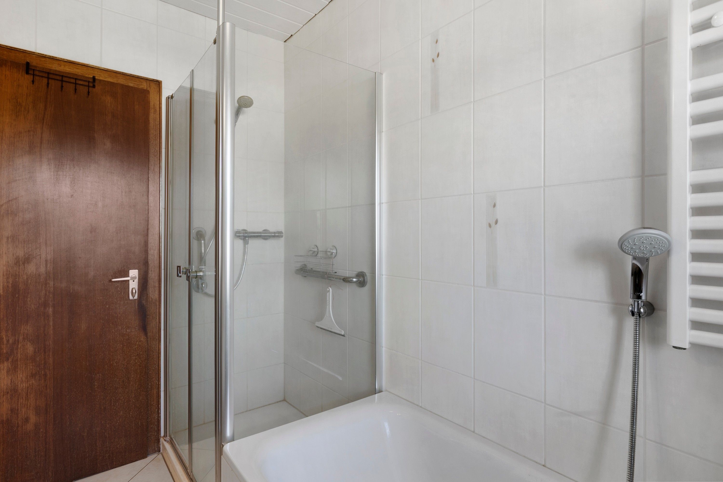 A bathroom with a glass-enclosed shower, a white bathtub, and a towel rack.