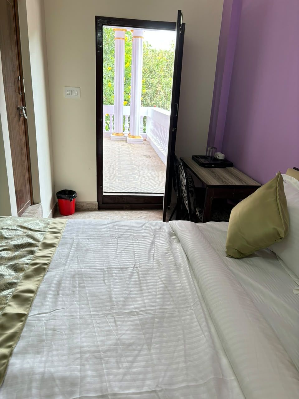 Una habitación de hotel con una cama, una mesita con una bandeja, un cesto de basura rojo y vistas al exterior.