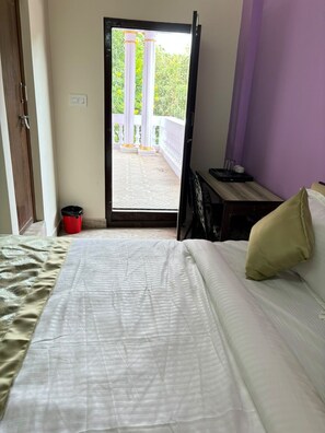 Una habitación de hotel con una cama, una mesita con una bandeja, un cesto de basura rojo y vistas al exterior.