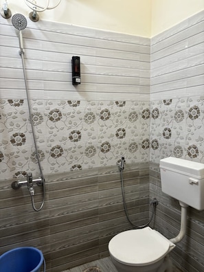A bathroom with a toilet, a shower, and a blue bucket. - Radha Shyam Residency & Convention Hall  (Mysore)
