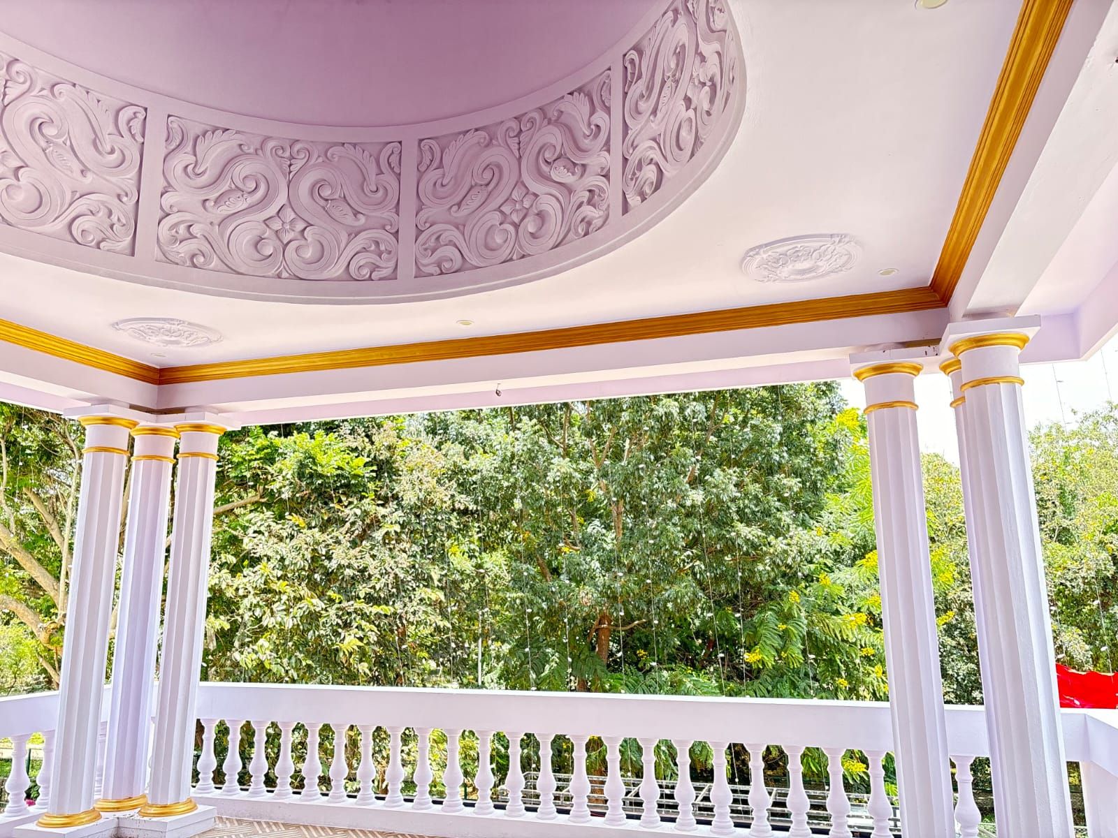 A gazebo with ornate ceiling and white columns with golden bases.
