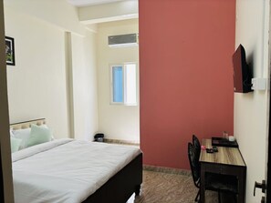 Habitación de hotel con cama, escritorio, silla, ventana y televisor montado en la pared.