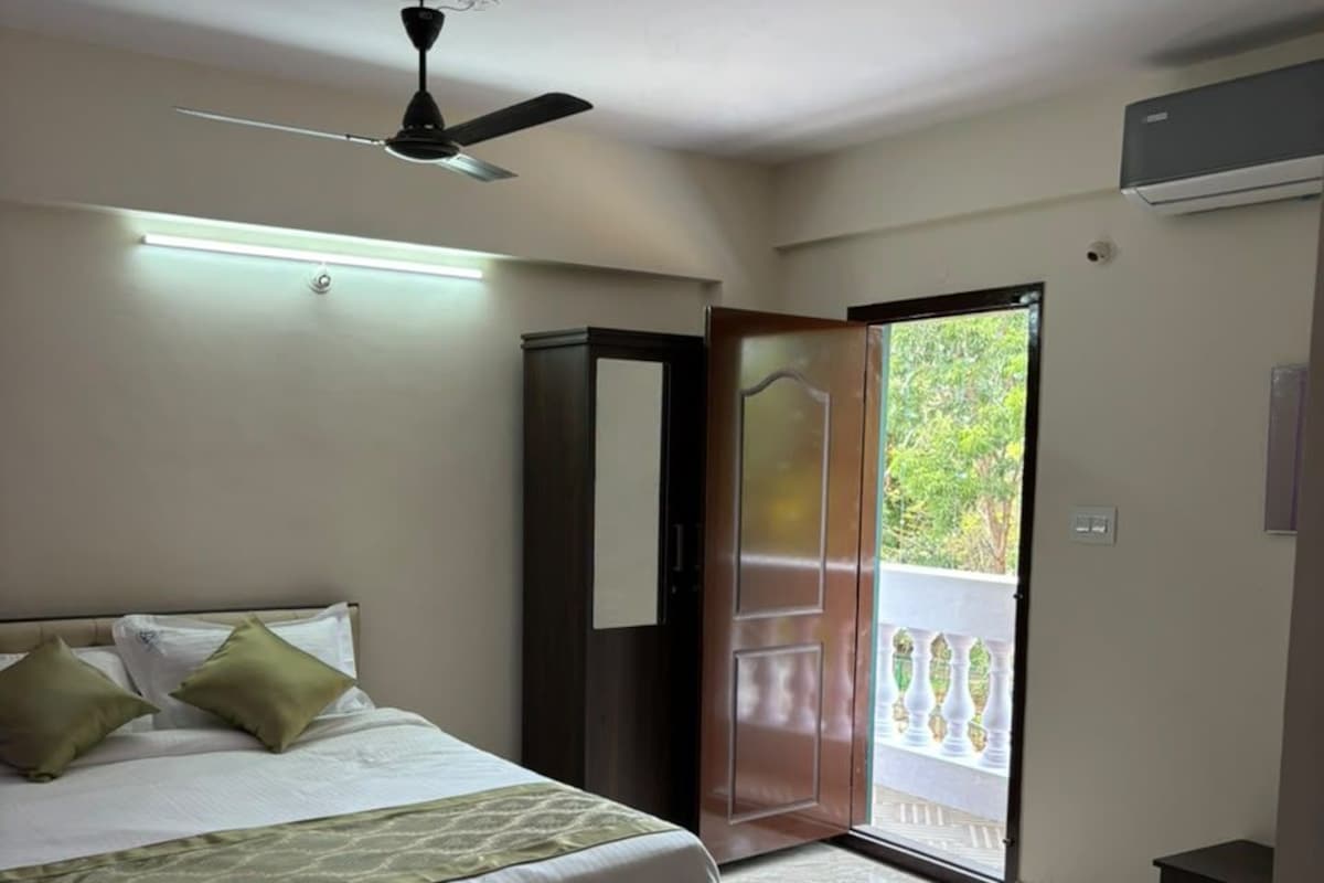 Un dormitorio con una cama, un ventilador de techo, una puerta que da a un balcón y una mesita de noche pequeña.