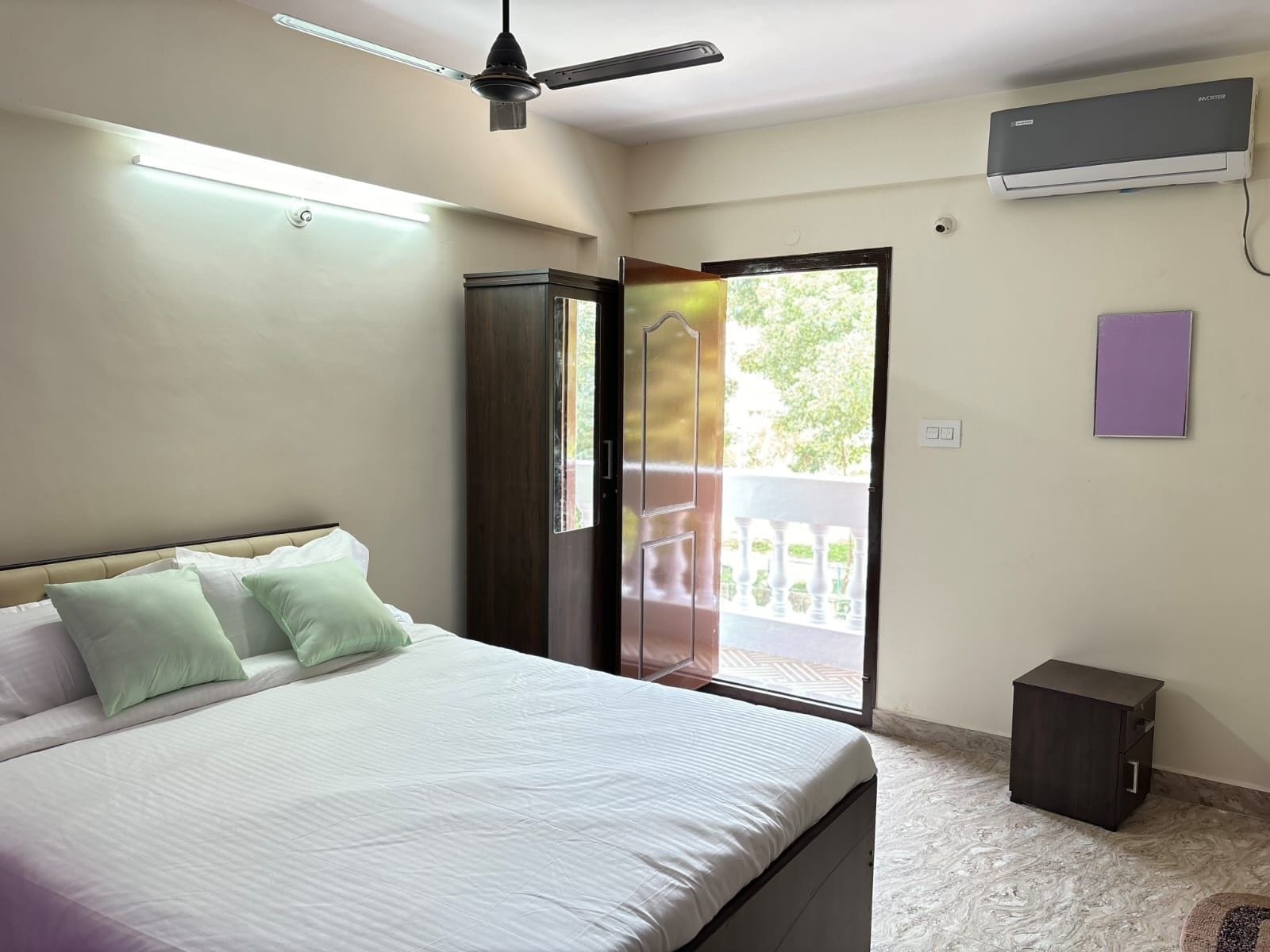 A bedroom with a bed, a ceiling fan, an air conditioning unit, a sliding glass door, and a small bedside table.