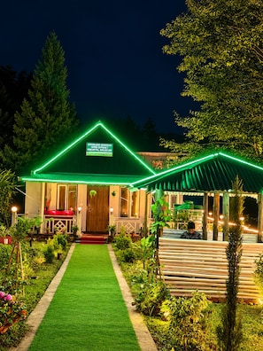 Un edificio con un letrero de neón verde, un jardín bien cuidado con césped y una terraza de madera.