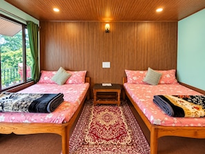 Habitación con dos camas, techo de madera, alfombra roja con estampado y una ventana con cortinas.