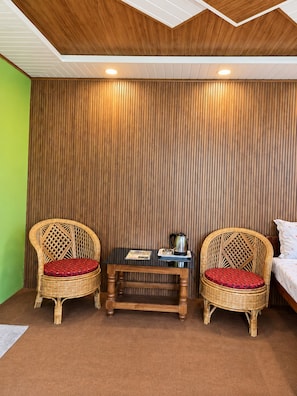 Una habitación con dos sillones de mimbre, una mesita de madera y una cama.