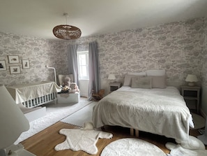 Ein Schlafzimmer mit einem Kinderbett, einem Bett, einer Pendelleuchte und einem Wandpapier mit Muster.