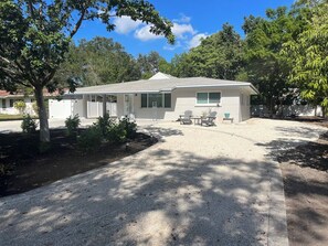 A single-story house with a covered porch, a gravel driveway, and a small patio area with outdoor furniture. - Downtown Sarasota House. Enjoy the Cultural side of area and 15 mins to Beach (Sarasota)