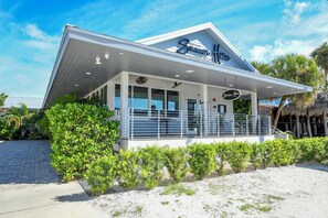 Un ristorante di pesce fronte spiaggia, con facciata bianca, ampie vetrate e una zona salotto all'aperto coperta.