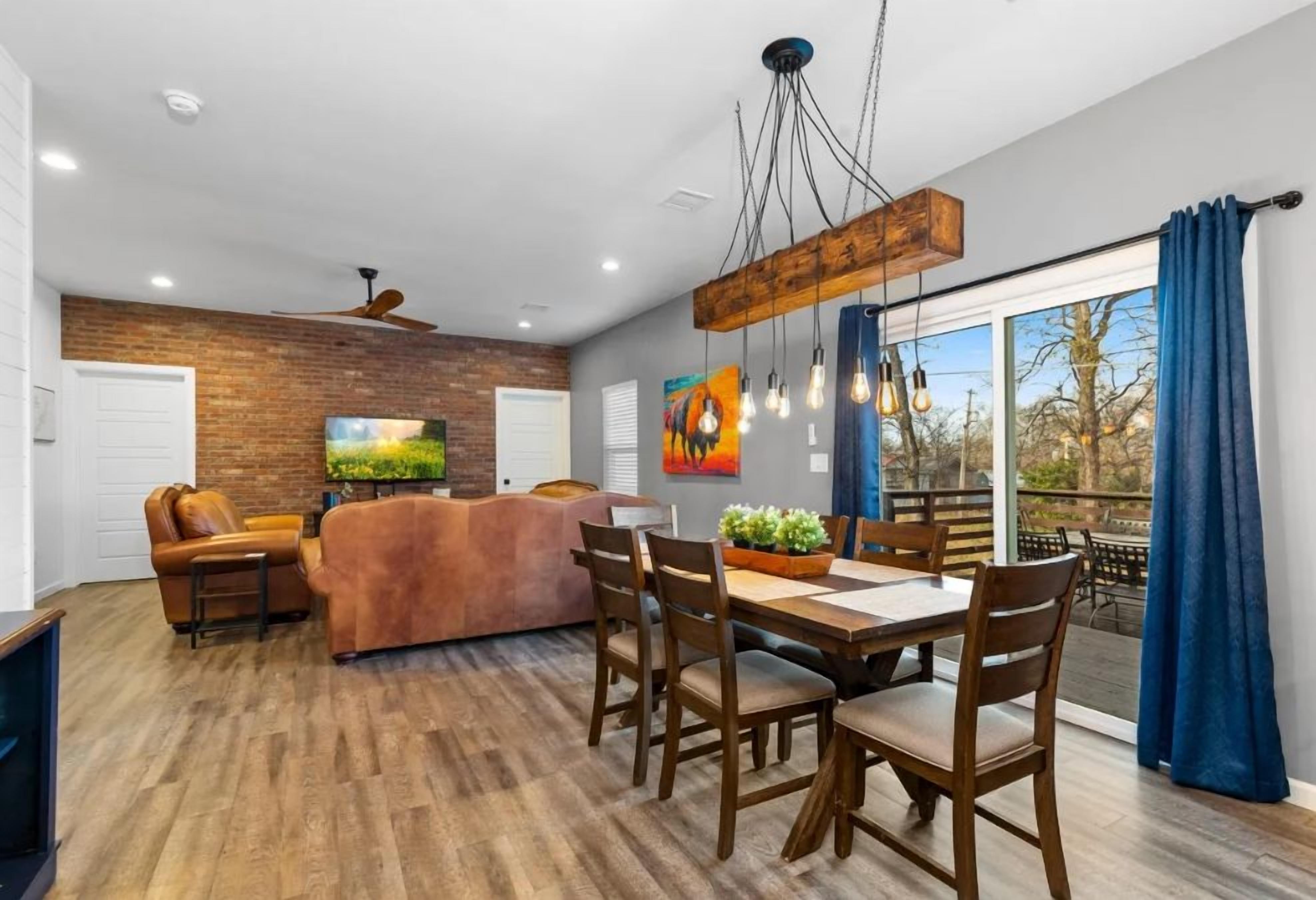 A modern living space with a dining area, a sofa, a TV, and a large window with curtains.