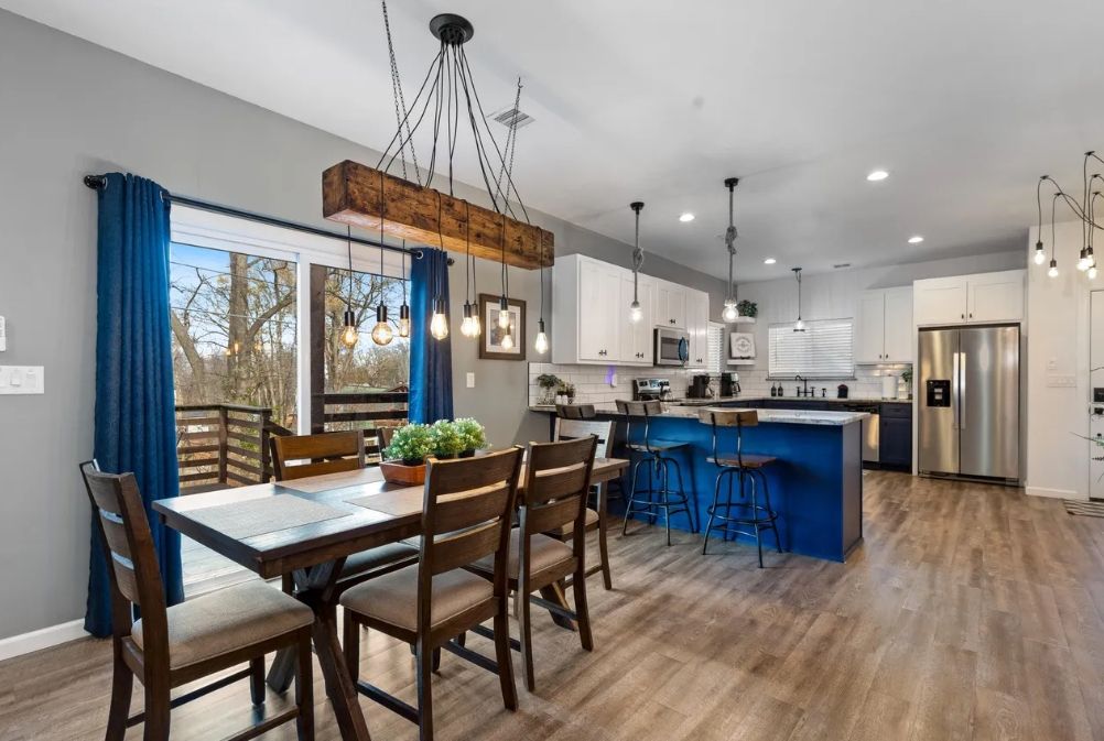 A modern kitchen with a central island, wooden chairs, and pendant lighting.