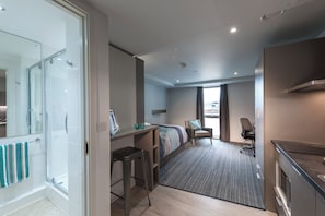 Ein Hotelzimmer mit Dusche, Schreibtisch, Bett und Stuhl, mit Blick auf die Stadt.