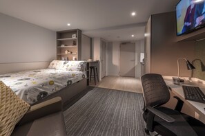 Un dormitorio moderno con cama, escritorio, silla y televisor.