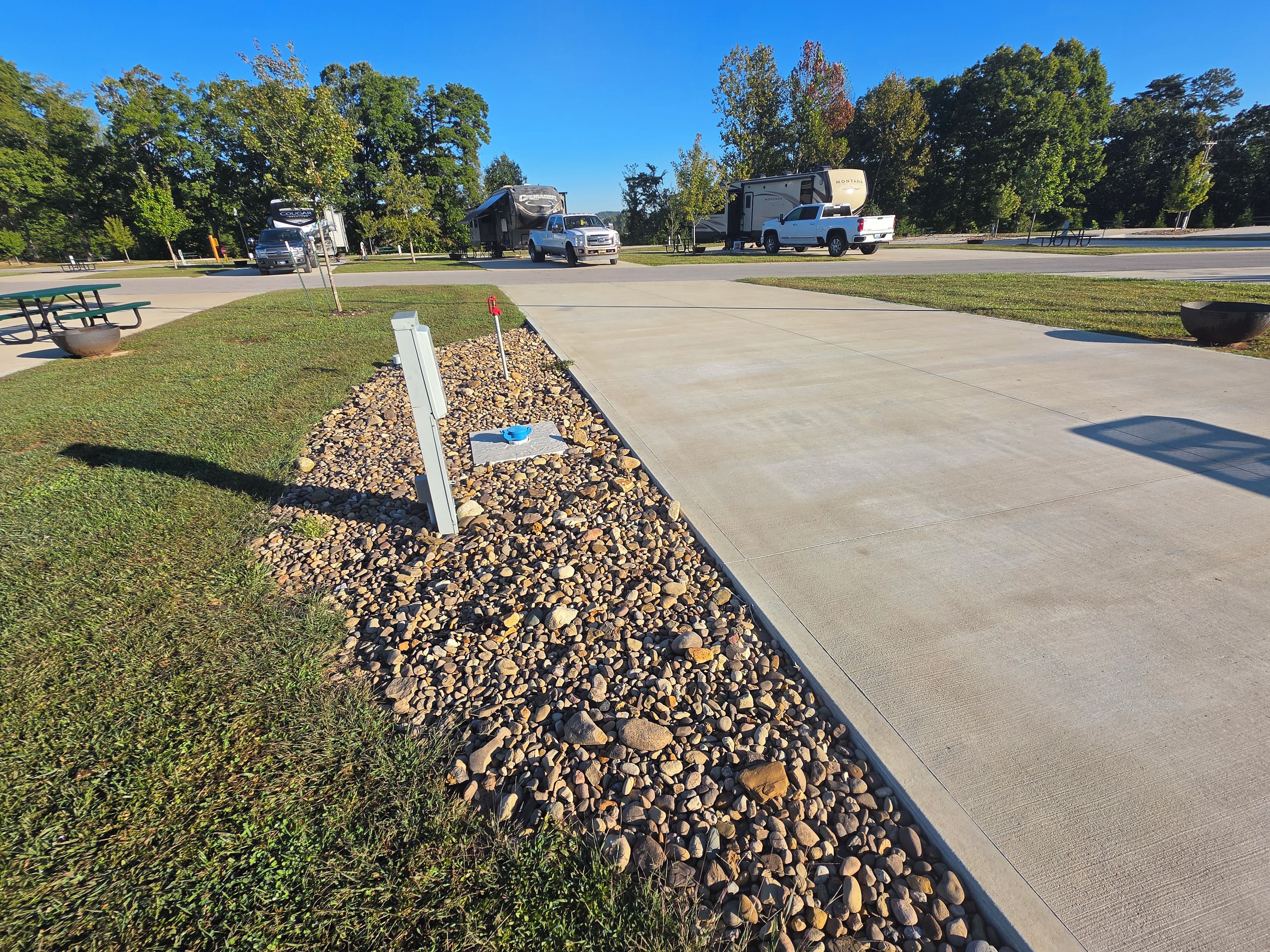 A paved walkway with a gravel border, picnic tables, and a camping trailer in the background.