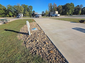 A paved walkway with a gravel border, picnic tables, and a camping trailer in the background.