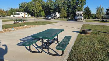 A picnic table with benches in a park area with RVs parked nearby.