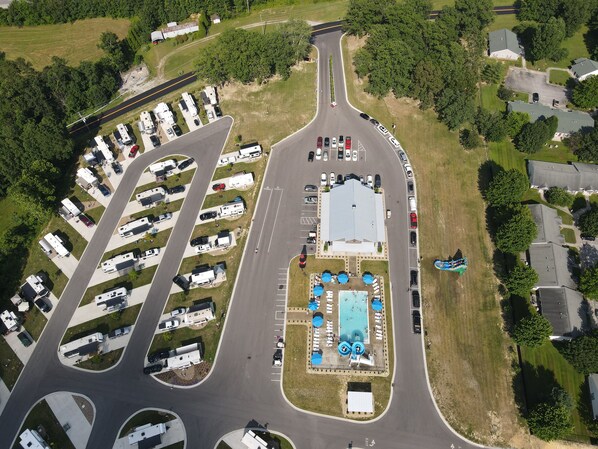 An aerial view of a campground with RV parking, a swimming pool, and a large building.
