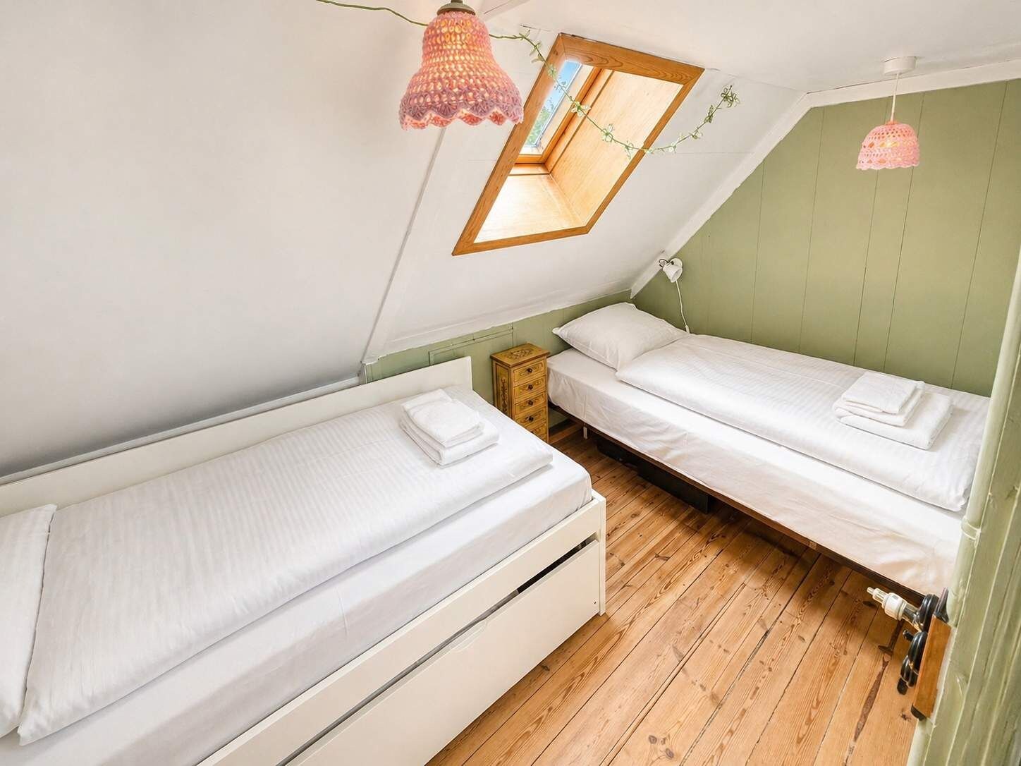 Une petite pièce agréable et chaleureuse, avec deux lits simples, un plancher en bois, une lucarne et une petite table.