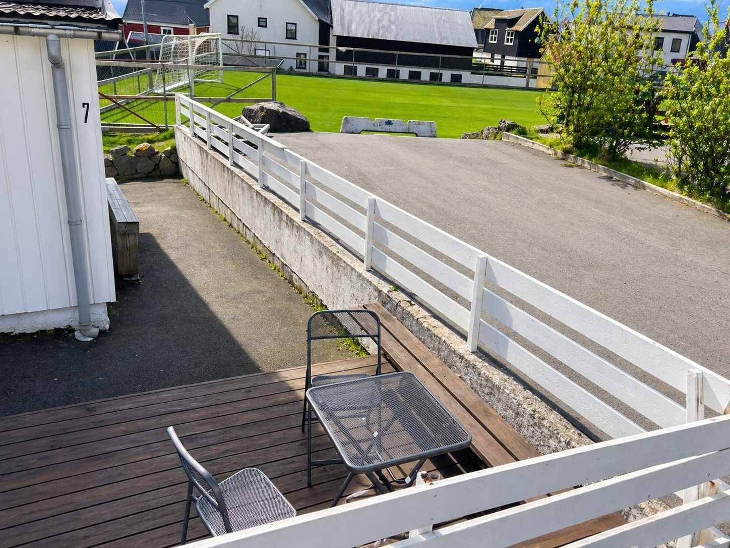 Une terrasse avec une table et des chaises donnant sur un terrain de sport.