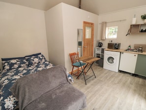 Ein kleines Zimmer mit einem Bett, einem Sessel, einer Waschmaschine und einer Küchenzeile.
