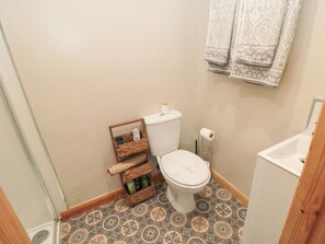 Ein kleines Badezimmer mit Toilette, einem Korb mit Pflegeprodukten und einem gemusterten Boden.