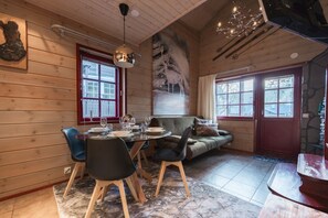 A cozy wooden interior with a dining table set for four, a sofa, and a large window with a view. - Levin Otava | Central 1BR Apt with Sauna & Balcony (Kittilä)
